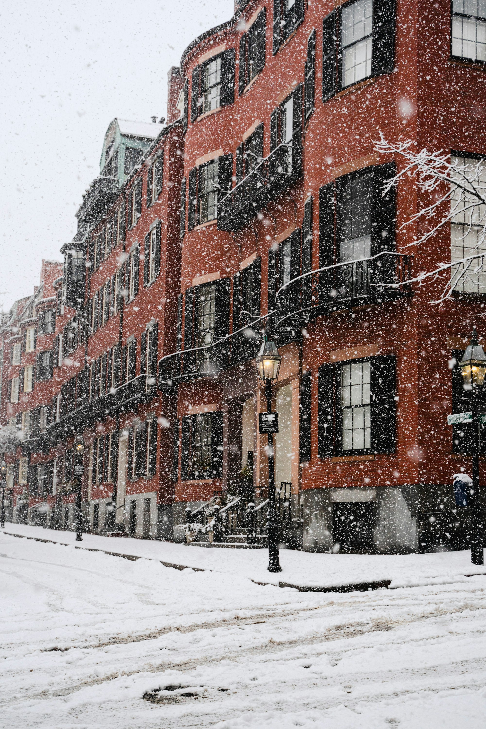 Boston brownstones under falling snow, gas lamps lit